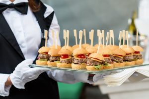 Catering service. Waiter carrying a tray of appetizers. Outdoor party with finger food, mini burgers, sliders.